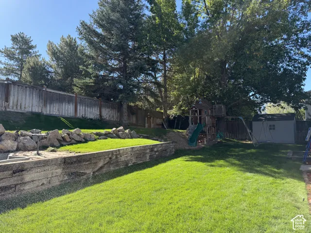 Expansive backyard featuring a tiered lawn, mature trees, wood retaining walls, and a wood privacy fence
