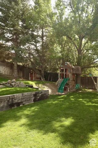 Expansive backyard featuring a manicured lawn, established mature trees and wooden play house with slide.