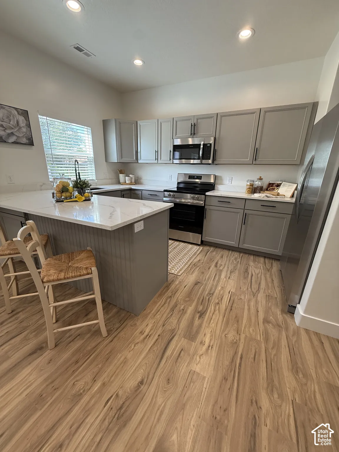 Kitchen featuring grey cabinetry, stainless steel appliances, wood-finish flooring, recessed lighting, and a kitchen island with a white countertop