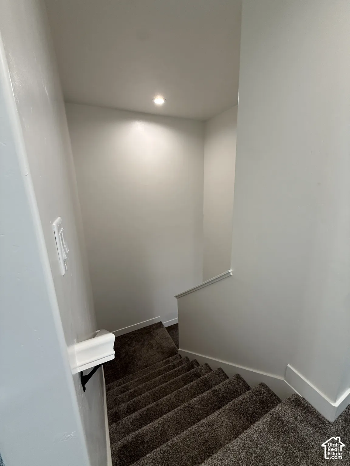 Carpeted staircase with contemporary wall lighting, white trim, and a white handrail