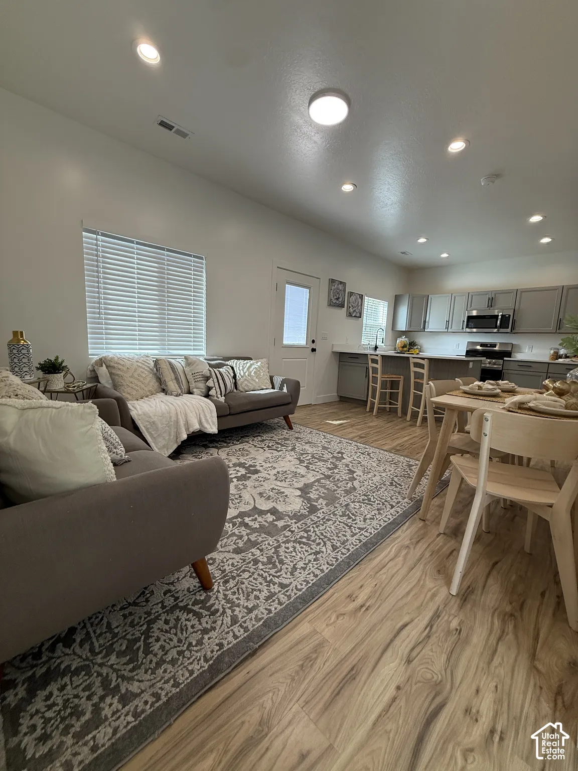 Open-concept living space featuring wood-finish flooring, recessed lighting, and a kitchen with gray cabinetry and stainless steel appliances