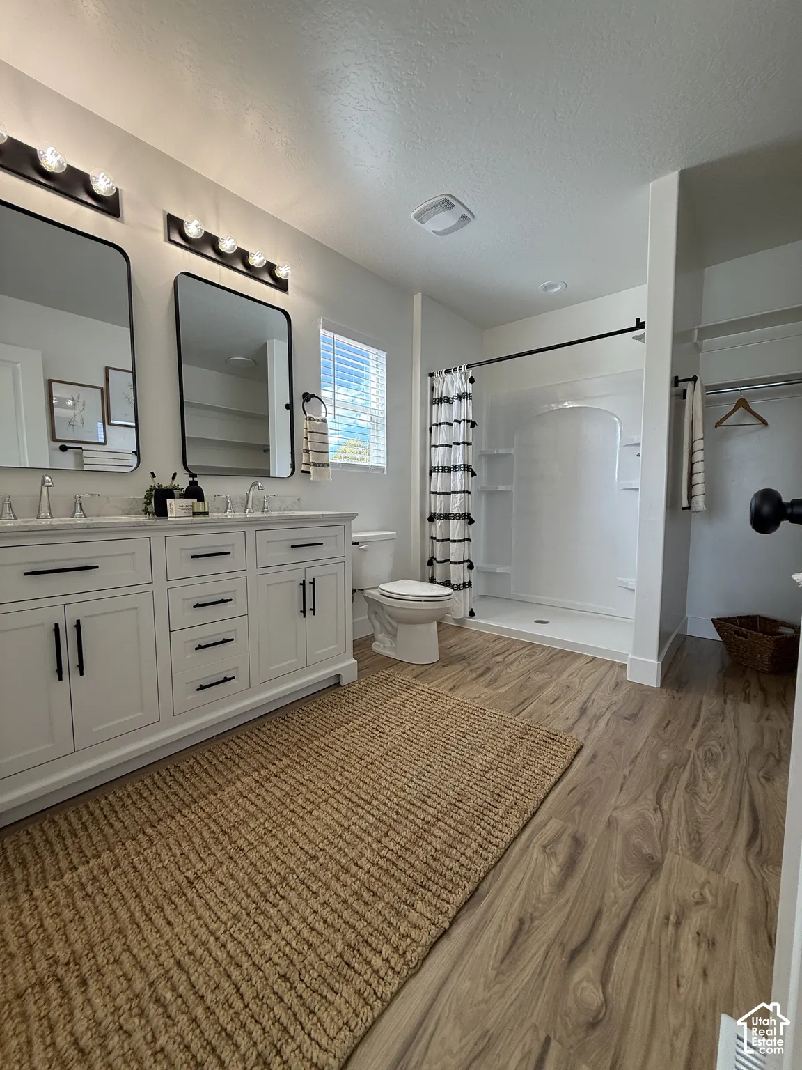 Dual vanity with white cabinetry, wood-finish flooring, a white shower enclosure, and modern black fixtures