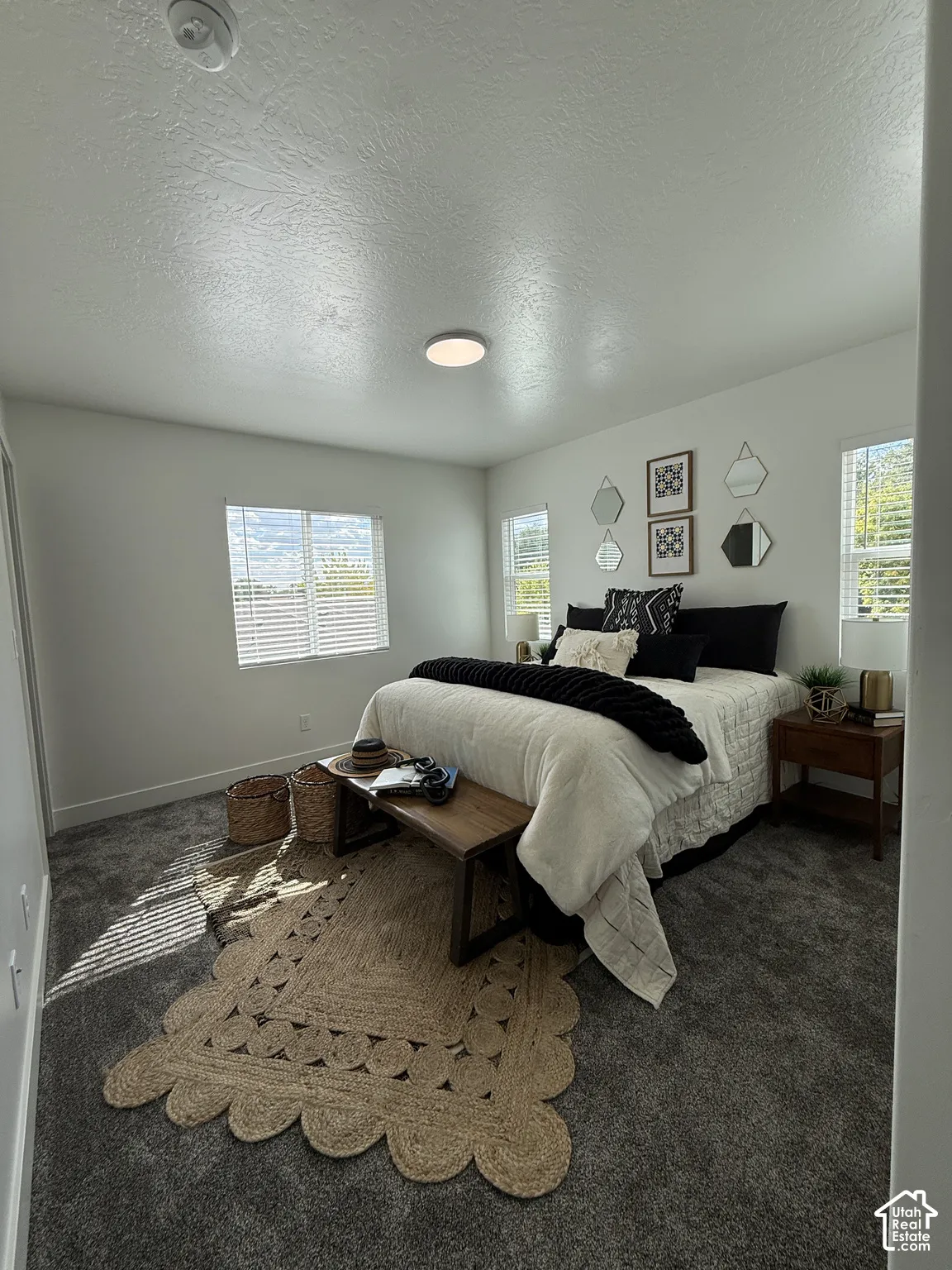 Neutral-toned walls, gray carpeting, a single ceiling light fixture, and two windows with blinds