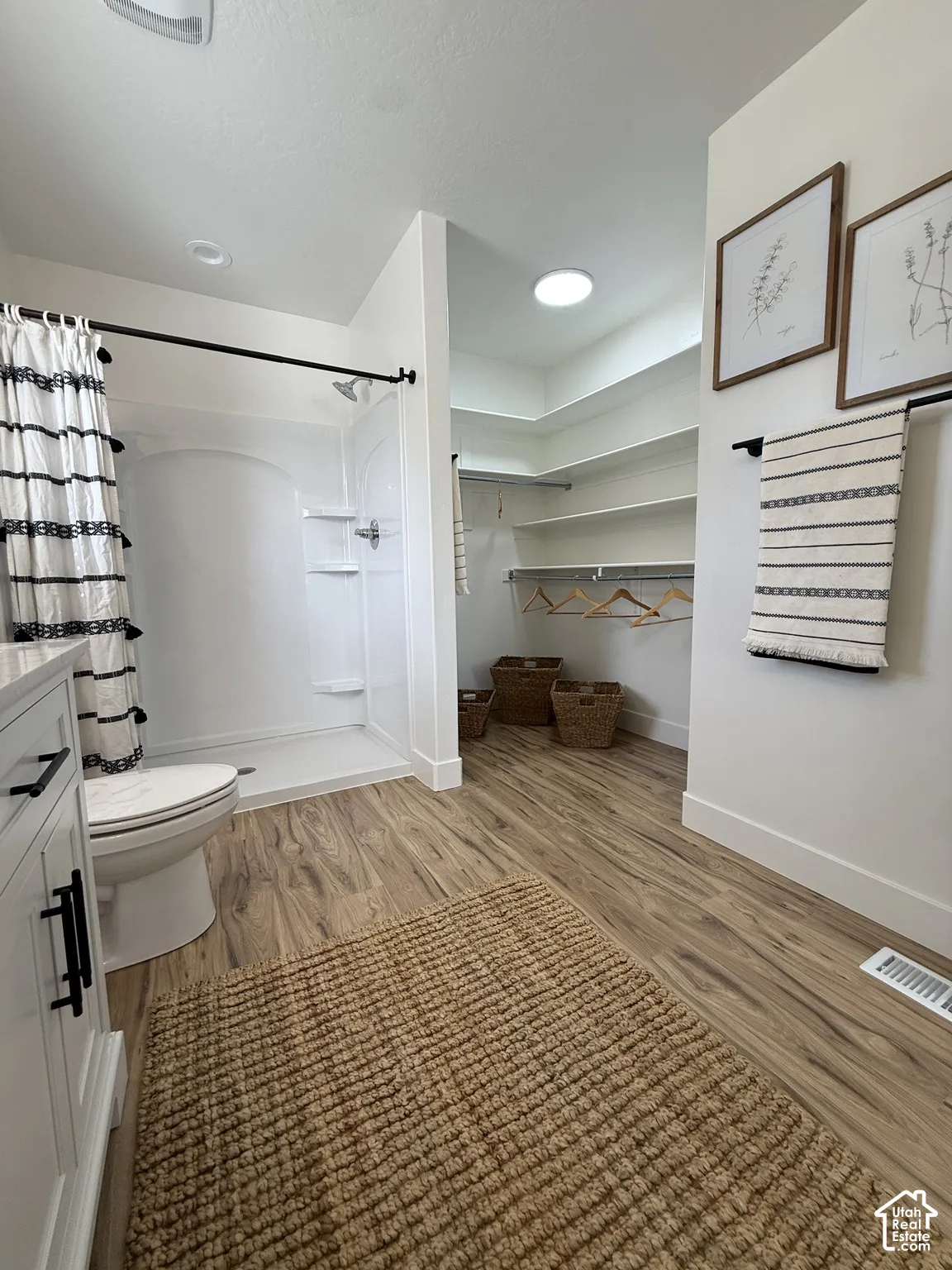 Wood-finish flooring, white vanity with matte black hardware, integrated shower/tub combination, and a walk-in closet with built-in shelving