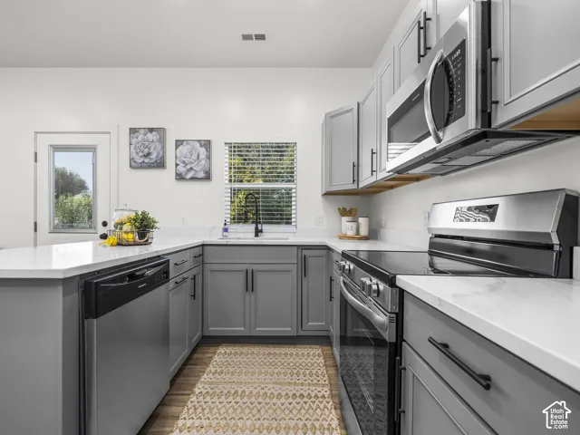 Kitchen featuring gray cabinetry, white countertops, stainless steel appliances, and wood-finish flooring