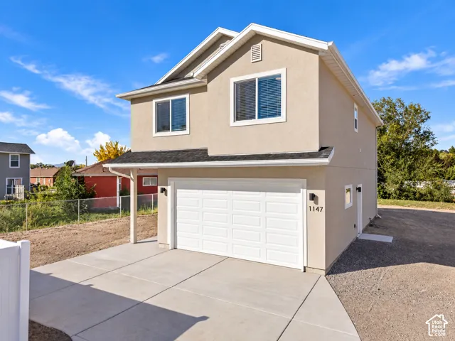 Two-story stucco exterior with white trim, two-car garage, concrete driveway, and black composition shingle roof
