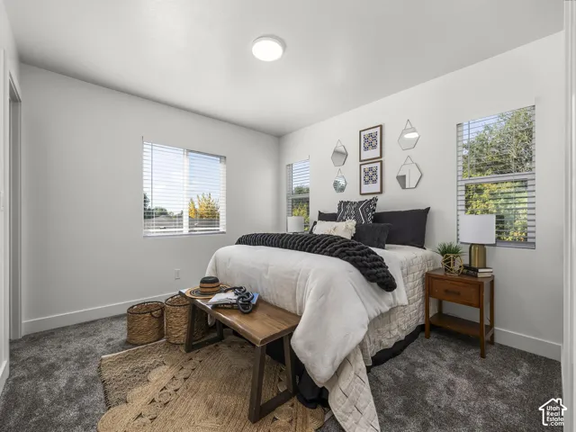 Recessed lighting, light gray wall color, multiple windows with blinds, gray carpet flooring, and a wood-finish bedside table