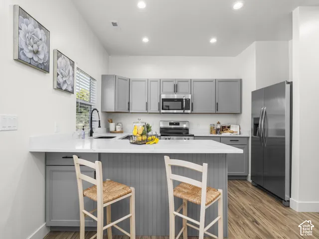 Kitchen featuring a central island with a breakfast bar, gray cabinetry, stainless steel appliances, white countertops, and wood-finish flooring