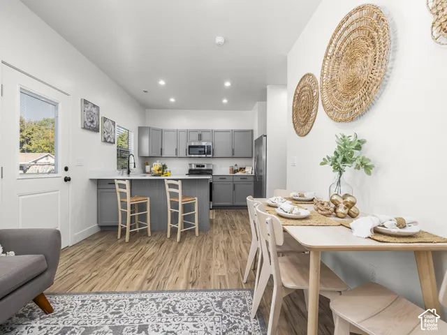 Open concept kitchen and dining area featuring wood-finish flooring, gray cabinetry, and a kitchen island with seating