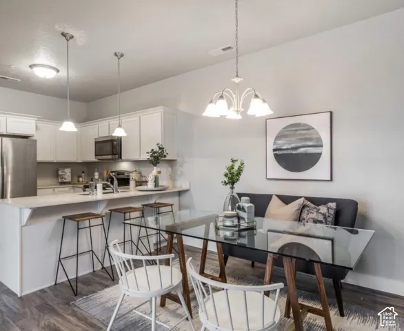 White shaker-style cabinetry, stainless steel appliances, pendant lighting, and wood-finish flooring