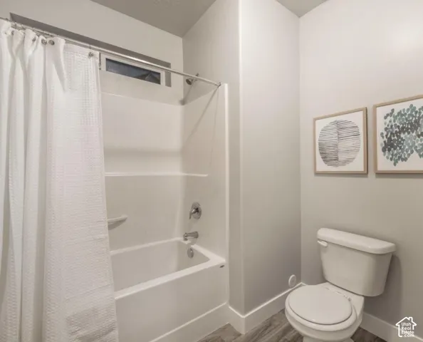 White tub and shower combination with chrome fixtures, wood-finish flooring, and a window above the shower