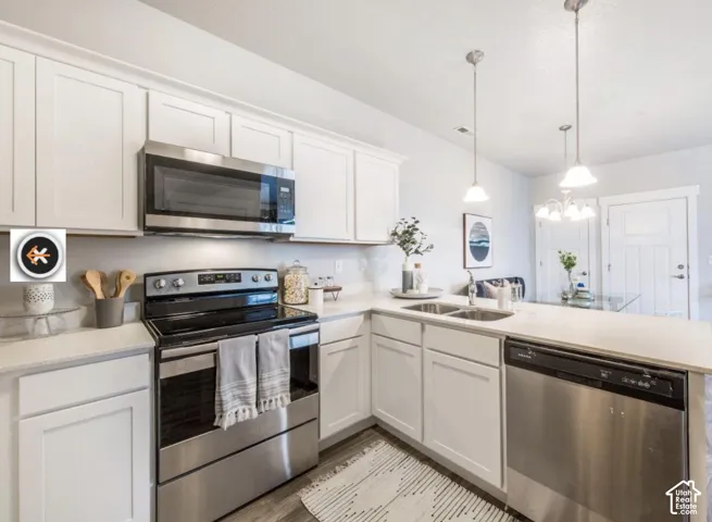 Kitchen featuring white shaker cabinetry, stainless steel appliances, light-toned countertops, and pendant lighting