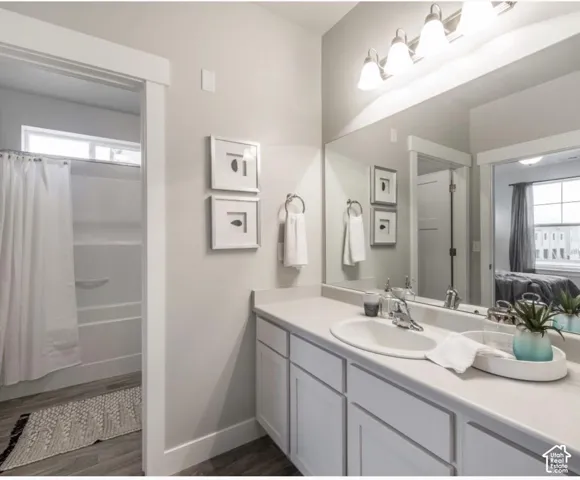 Bathroom featuring a white vanity with an undermount sink, a large wall-mounted mirror, and wood-finish flooring