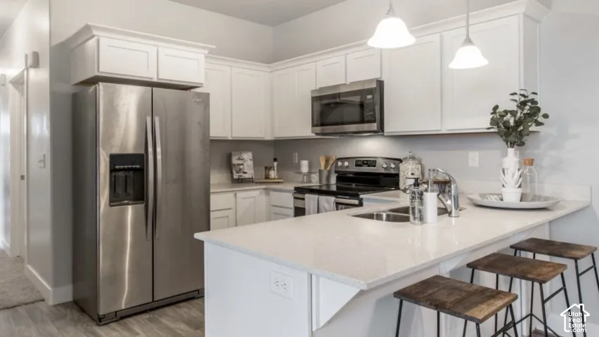 White shaker cabinetry, stainless steel appliances, light-toned countertops, and pendulum lighting