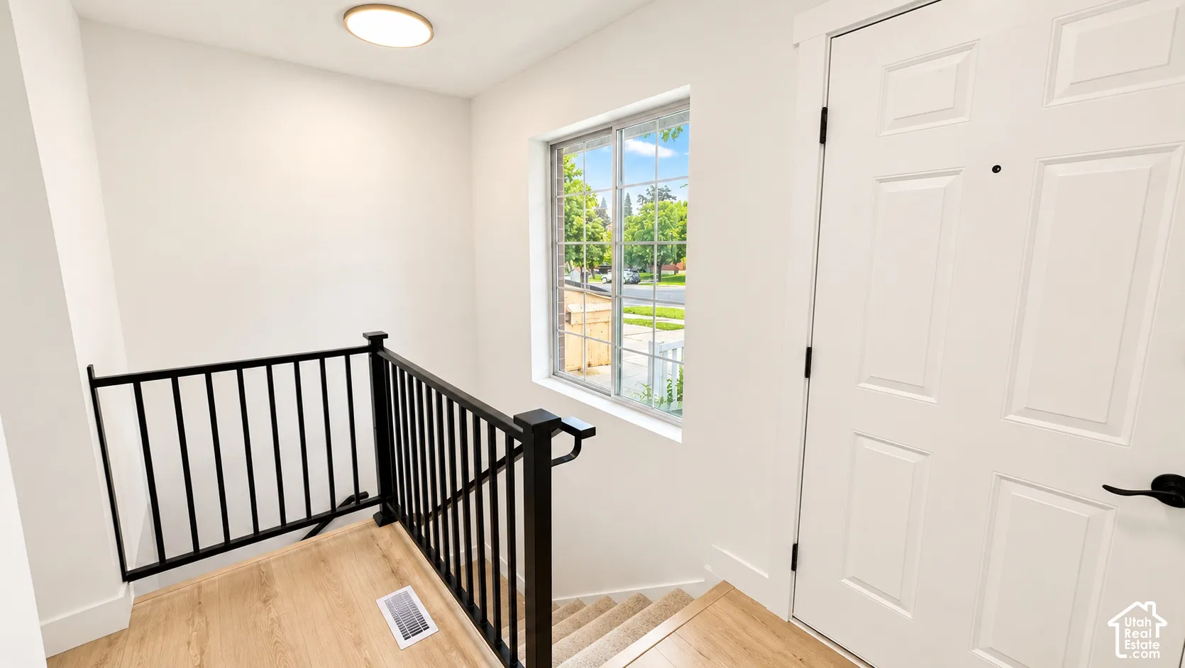 White paneled interior door with matte black hardware, wood-finish flooring, and a window with white trim