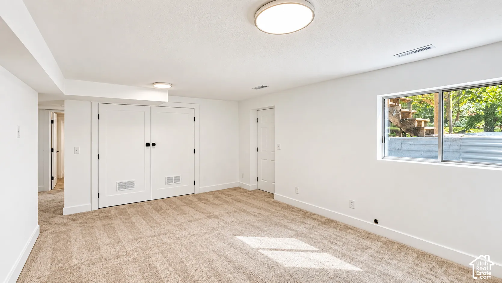 Light-colored carpeting, white walls, and a window with a wood-framed exterior structure