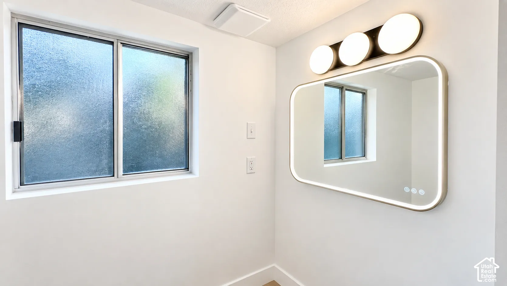 Frosted glass window, integrated LED mirror, modern vanity lighting, white painted walls, and ceiling-mounted exhaust fan