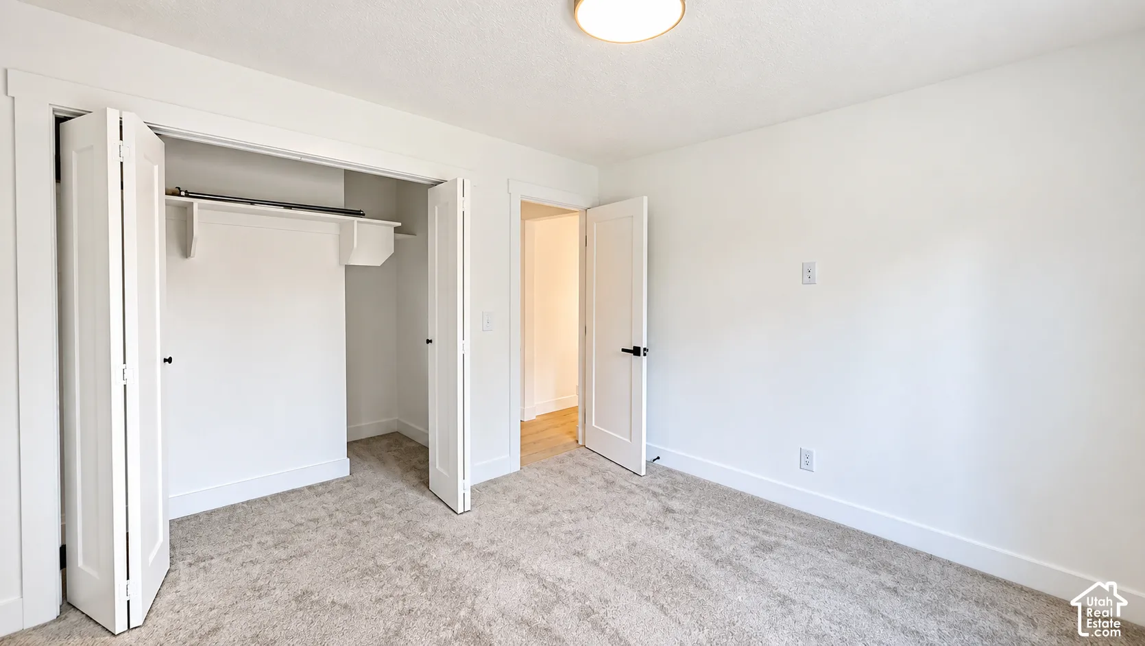 Light-toned carpeting and white walls with a built-in closet featuring bi-fold doors