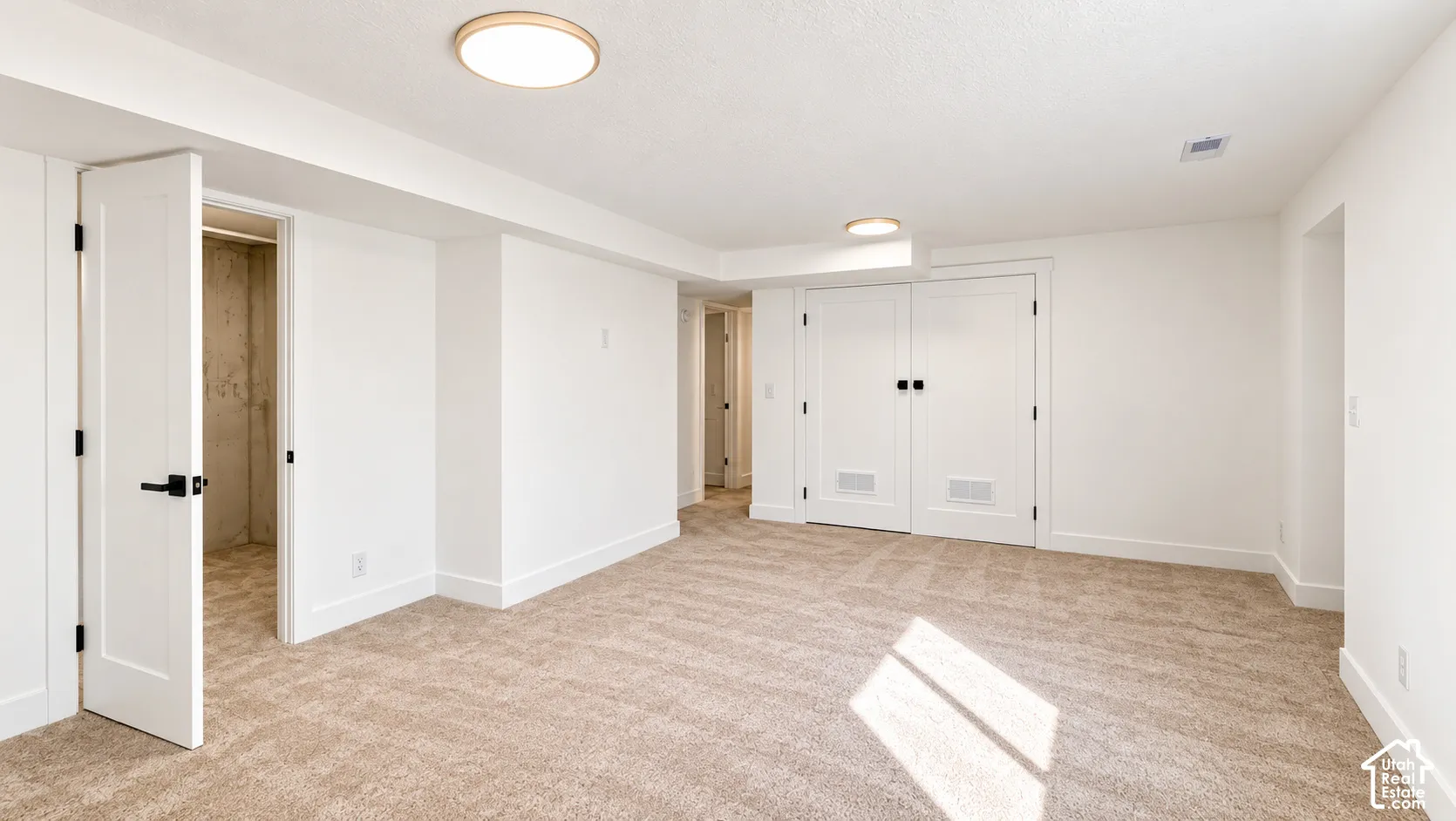 Carpeted flooring, contemporary flush-mount lighting, clean white walls, a white paneled door with matte black hardware, and double white paneled closet doors with matte black hardware