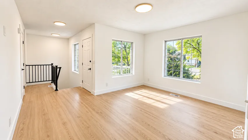 Spacious room featuring wood-finish flooring, multiple windows, a white paneled door, and a black metal staircase railing