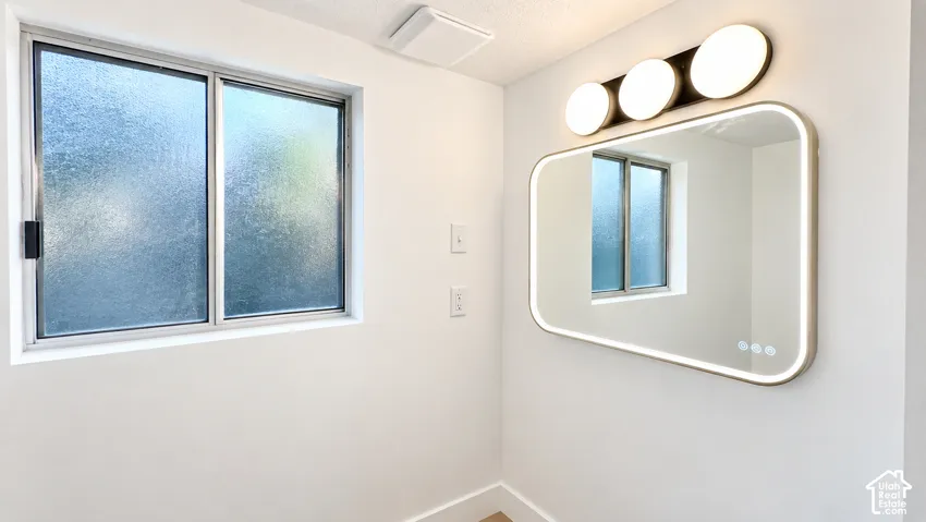 Frosted glass window, integrated LED mirror, modern vanity lighting, white painted walls, and ceiling-mounted exhaust fan