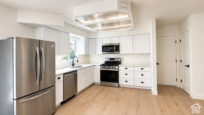 White shaker cabinetry, stainless steel appliances, light-toned wood-finish flooring, white countertops, and a black faucet and hardware