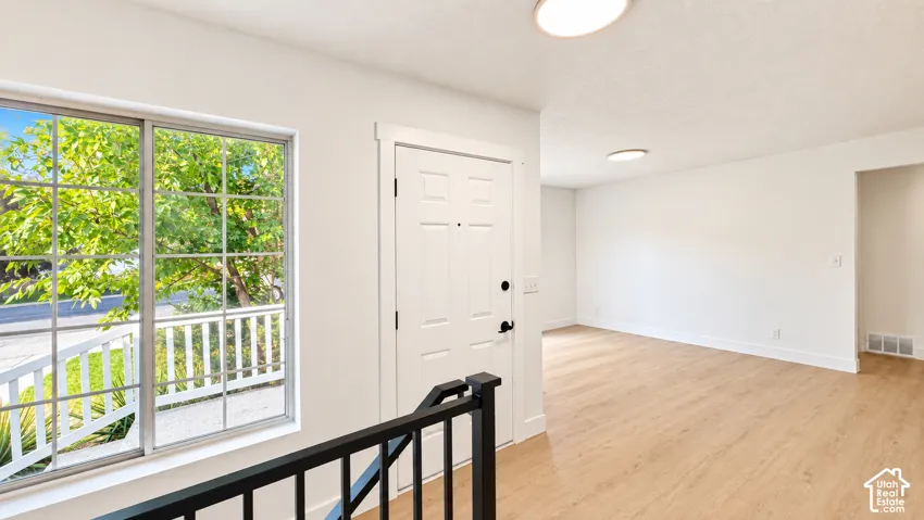 Wood-finish flooring, white paneled door, black metal railing, overhead lighting, and large window