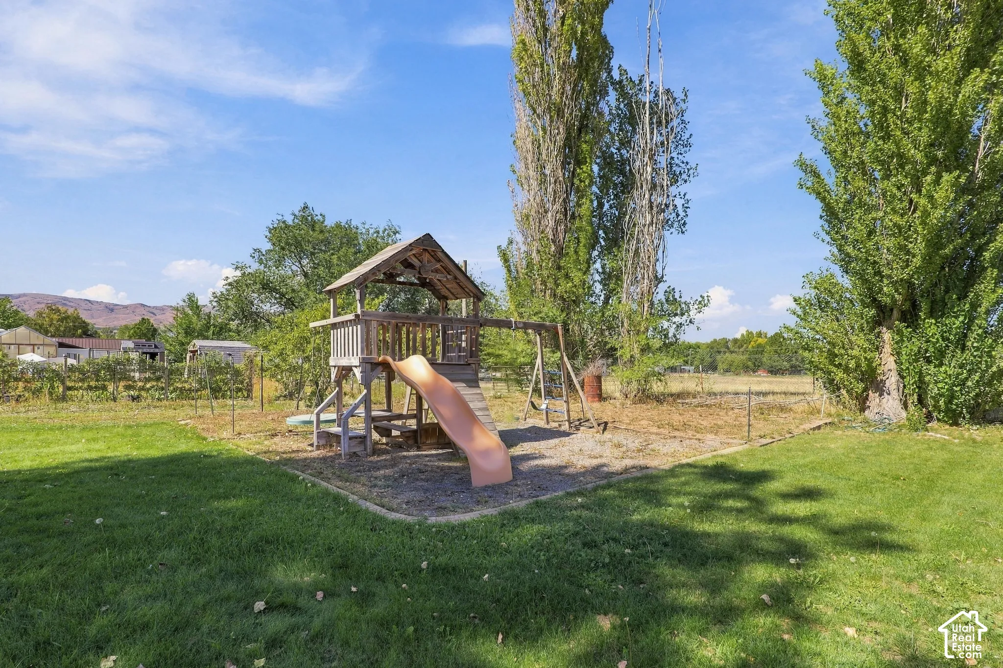 Expansive lawn area with a wooden playset featuring a slide and swings