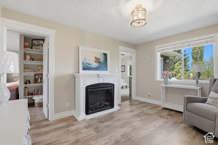 Focal fireplace with white surround, wood-finish flooring, ceiling-mounted light fixture, and an expansive window