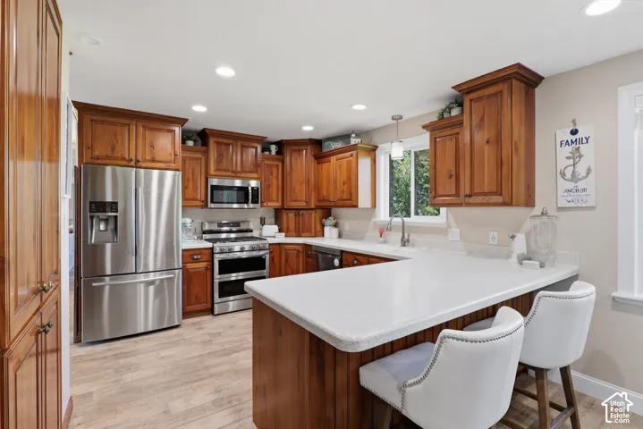 Kitchen featuring wood-finish cabinetry, stainless steel appliances, light-colored countertops, recessed lighting, and wood-finish flooring