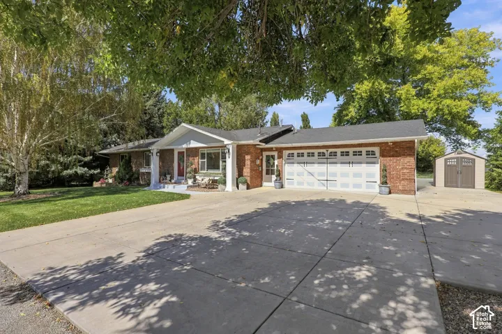 Brick exterior with white trim, two-car garage, concrete driveway, covered front porch, and an exterior shed