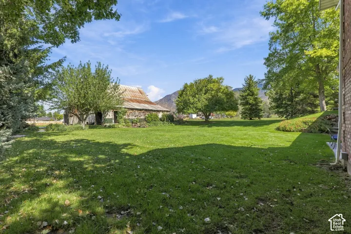 Expansive lawn area with mature trees, a rustic outbuilding, and a backdrop of distant mountains