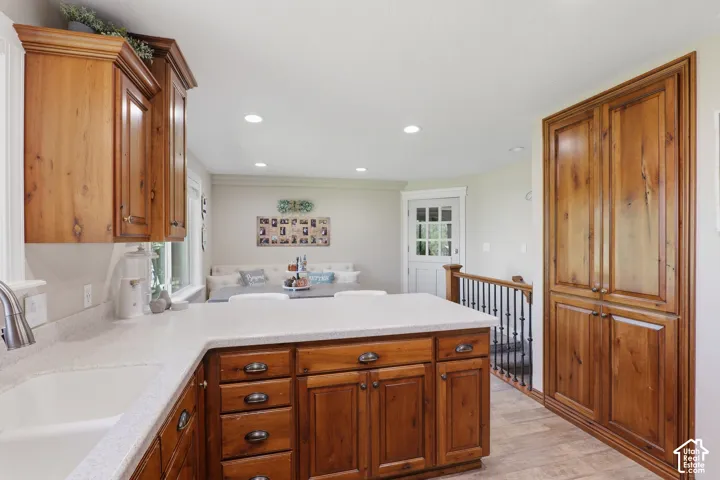 Wood cabinetry, white countertop, integrated sink, recessed lighting, and wood-finish flooring