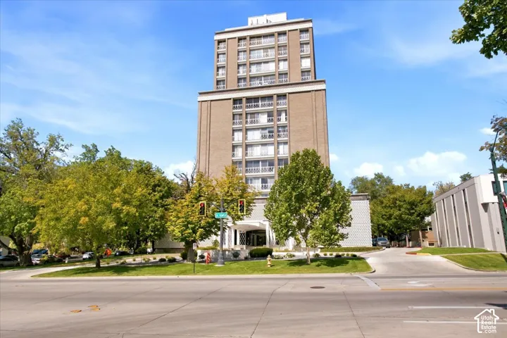 Multi-story building featuring a brick facade with multiple balconies, a covered entrance, and mature landscaping