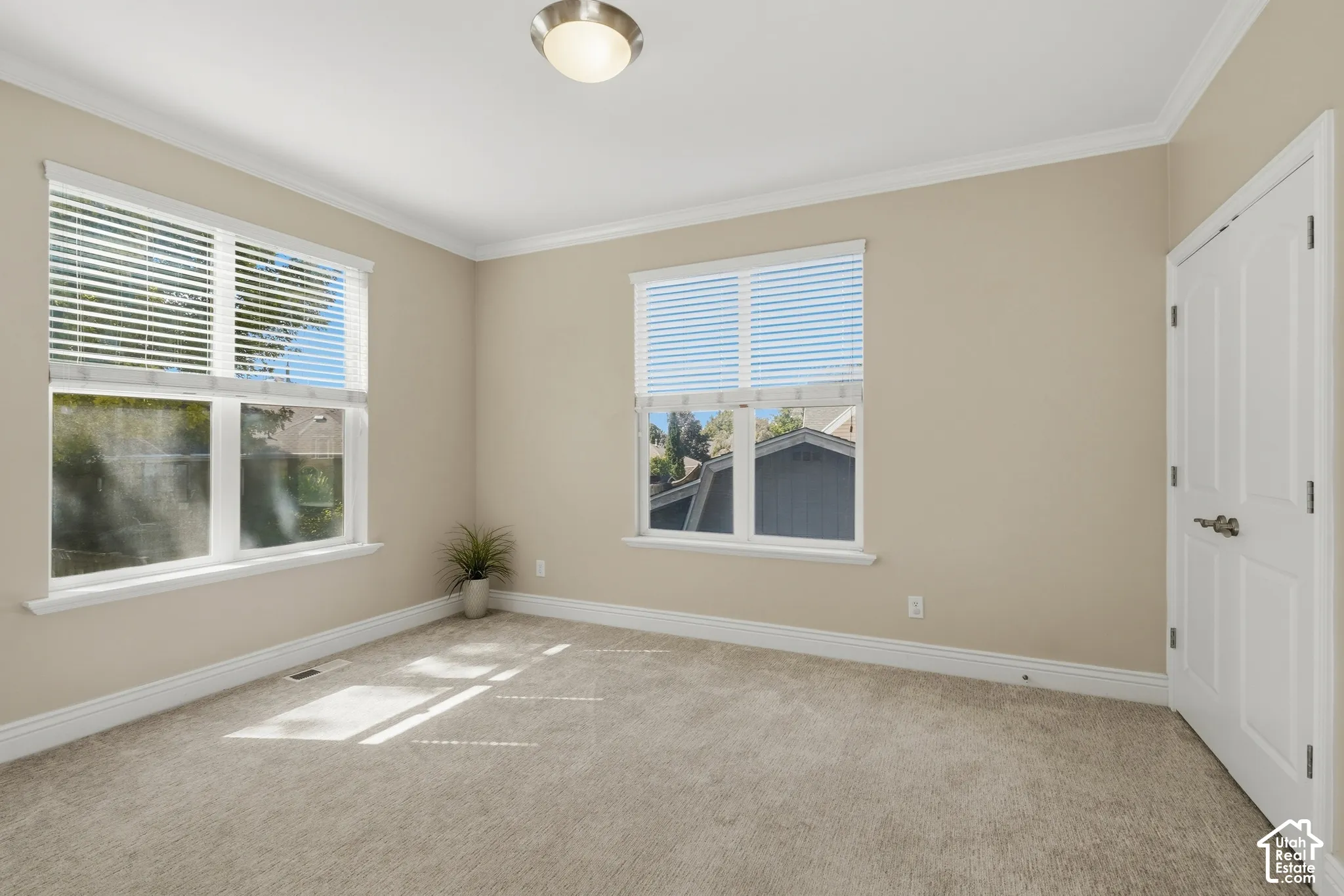 Neutral tone wall paint, crown molding, white trim, two windows with blinds, and a paneled door with brushed metal hardware