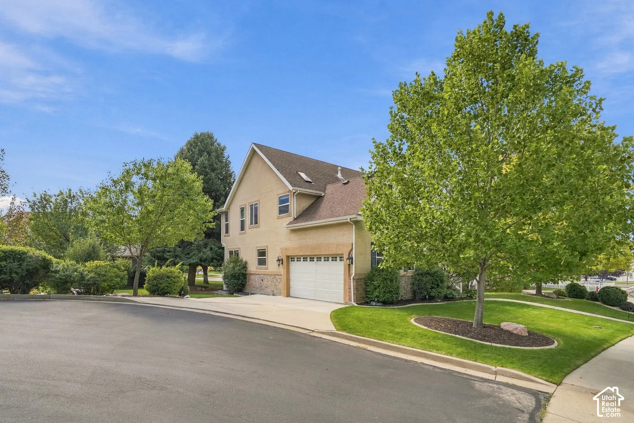 Two-story stucco exterior with stone accents, attached garage, sloped roof, and mature landscaping