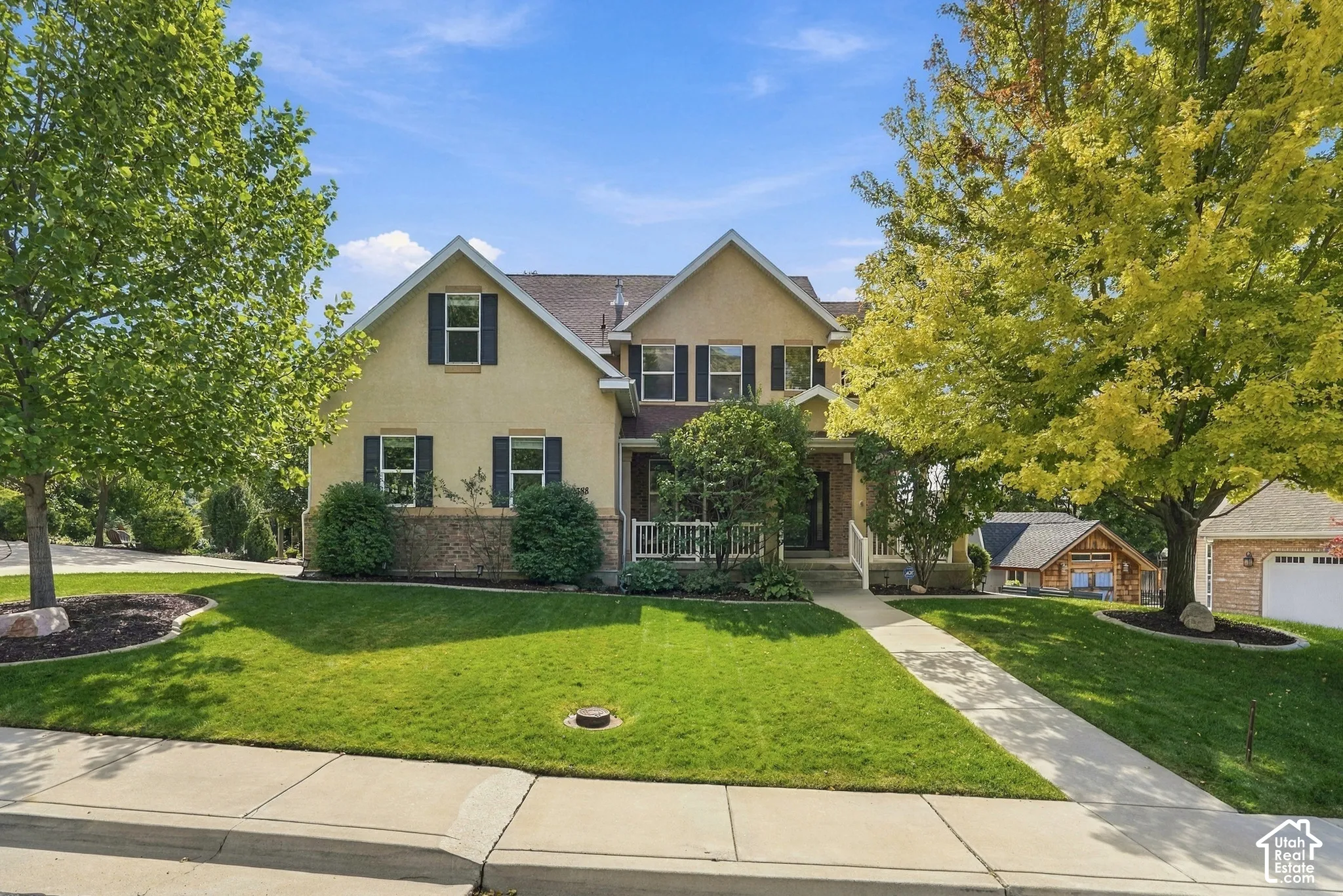 Two-story residence featuring a stucco and stone veneer exterior, a gabled roof, and a covered front porch with white railing
