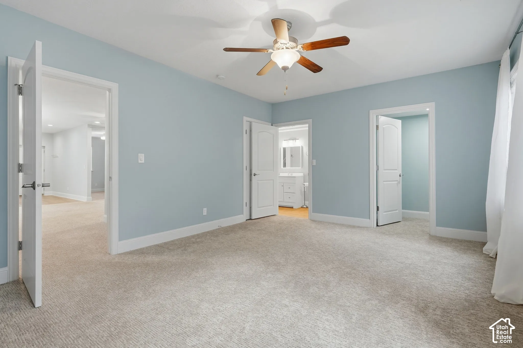 Ceiling fan with light fixture, light blue wall paint, white trim throughout, textured carpet flooring, white door with dark hardware