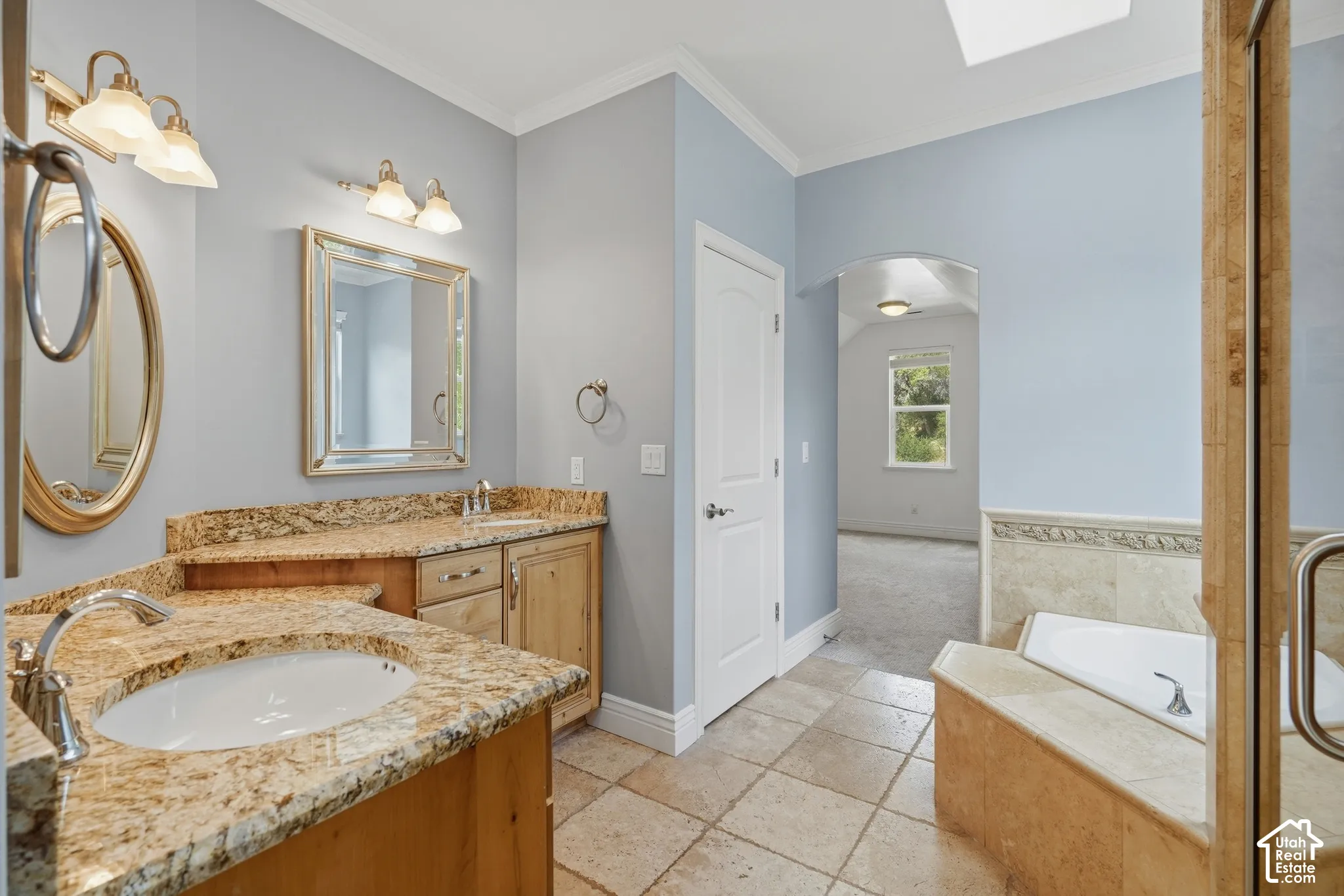 Dual vanities with stone countertops, tile flooring, built-in bathtub, and an arched doorway