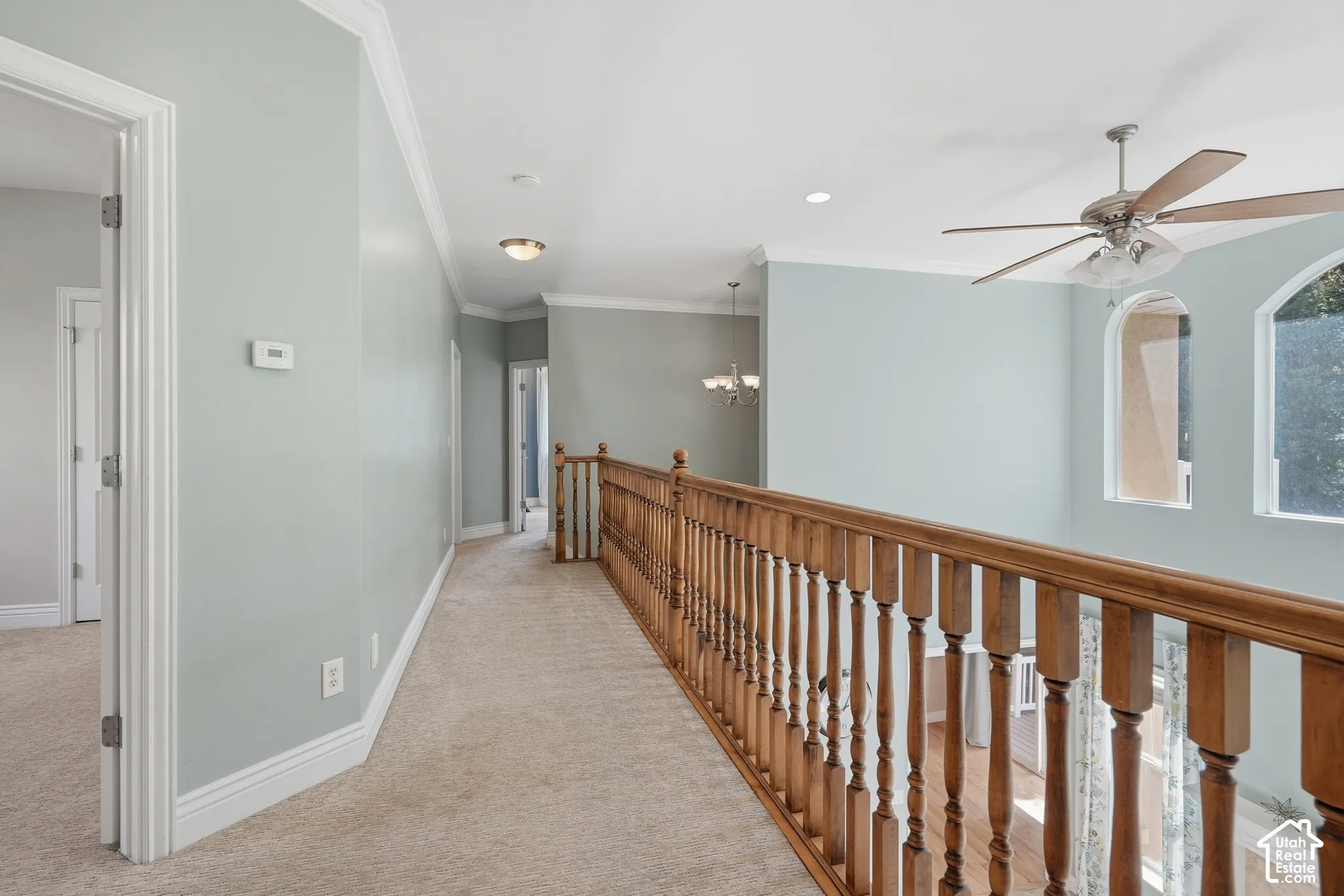 Carpeted hallway with wood banister, arched windows, ceiling fan, and recessed lighting