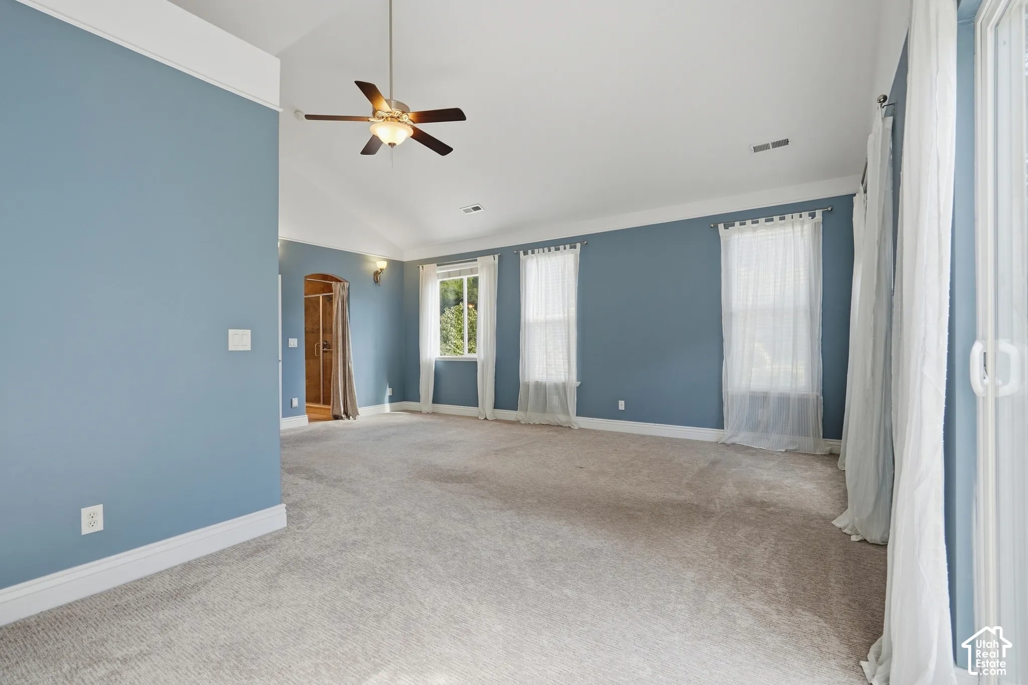 Vaulted ceiling with a ceiling fan, light blue walls, multiple windows, and light-colored carpeting