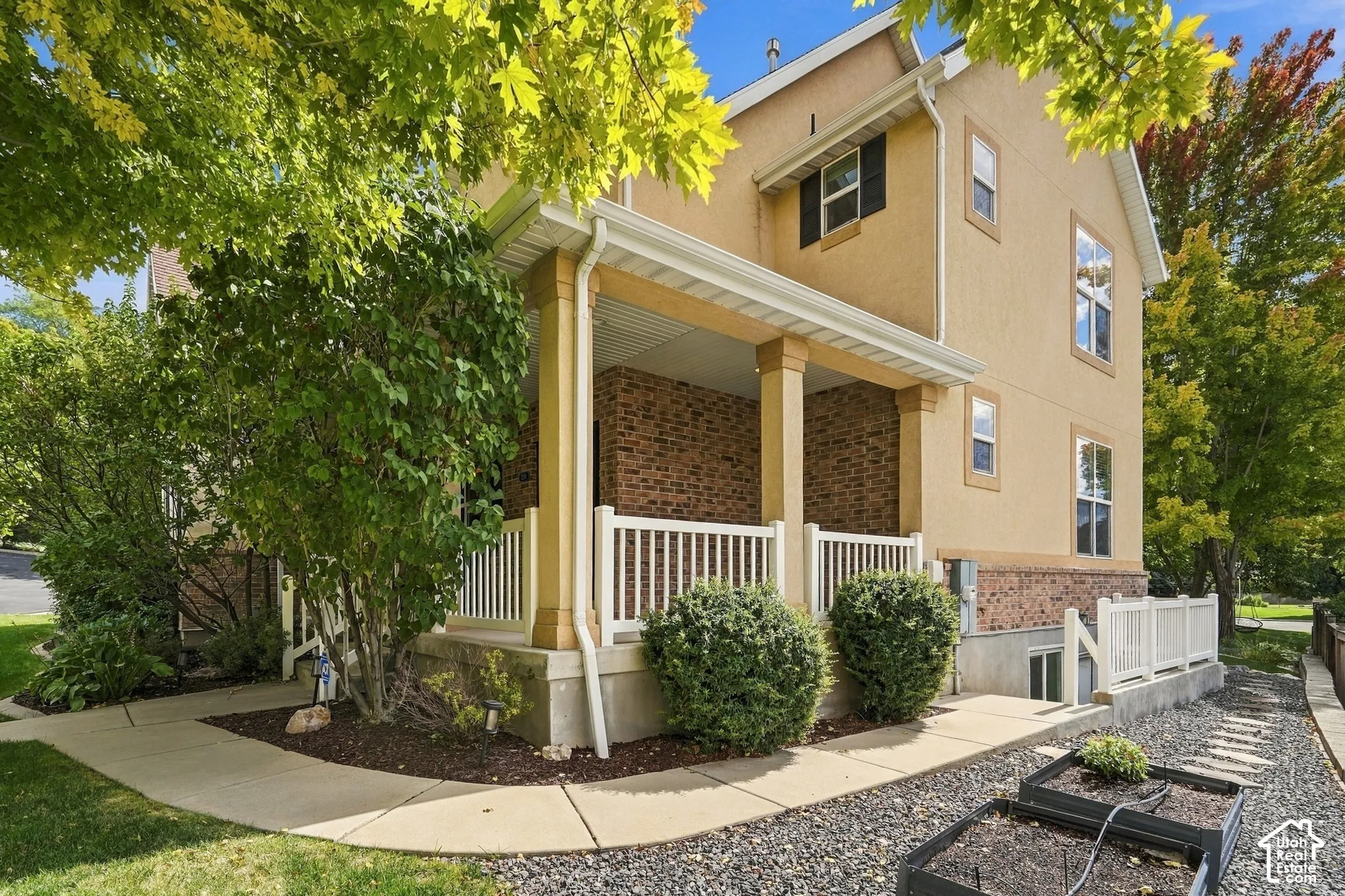 Stucco exterior with brick detailing, covered porch with white railing, established landscaping, and a side pathway