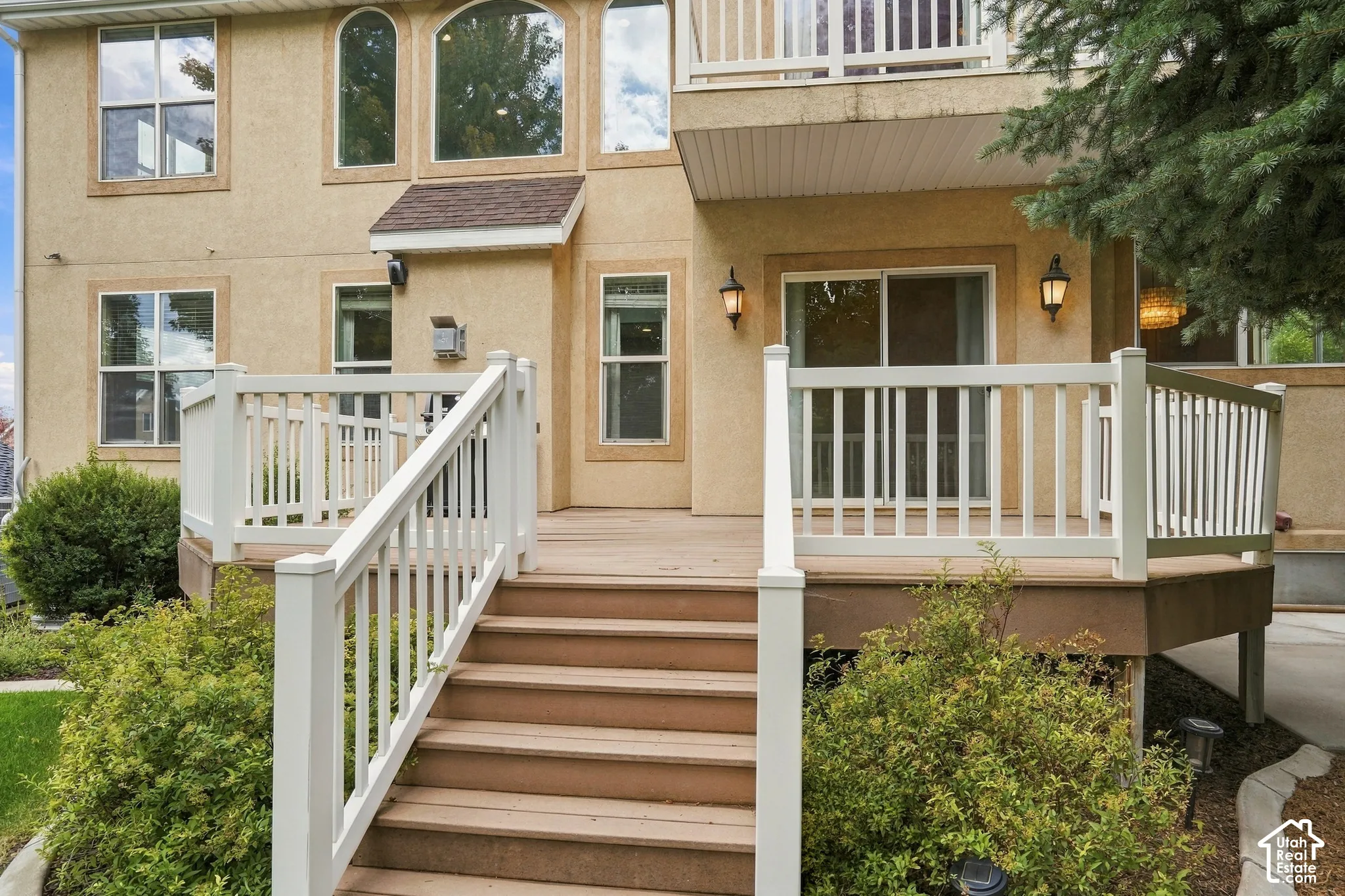 Multi-level deck with white railings and exterior lighting, featuring a sliding glass door and arched windows