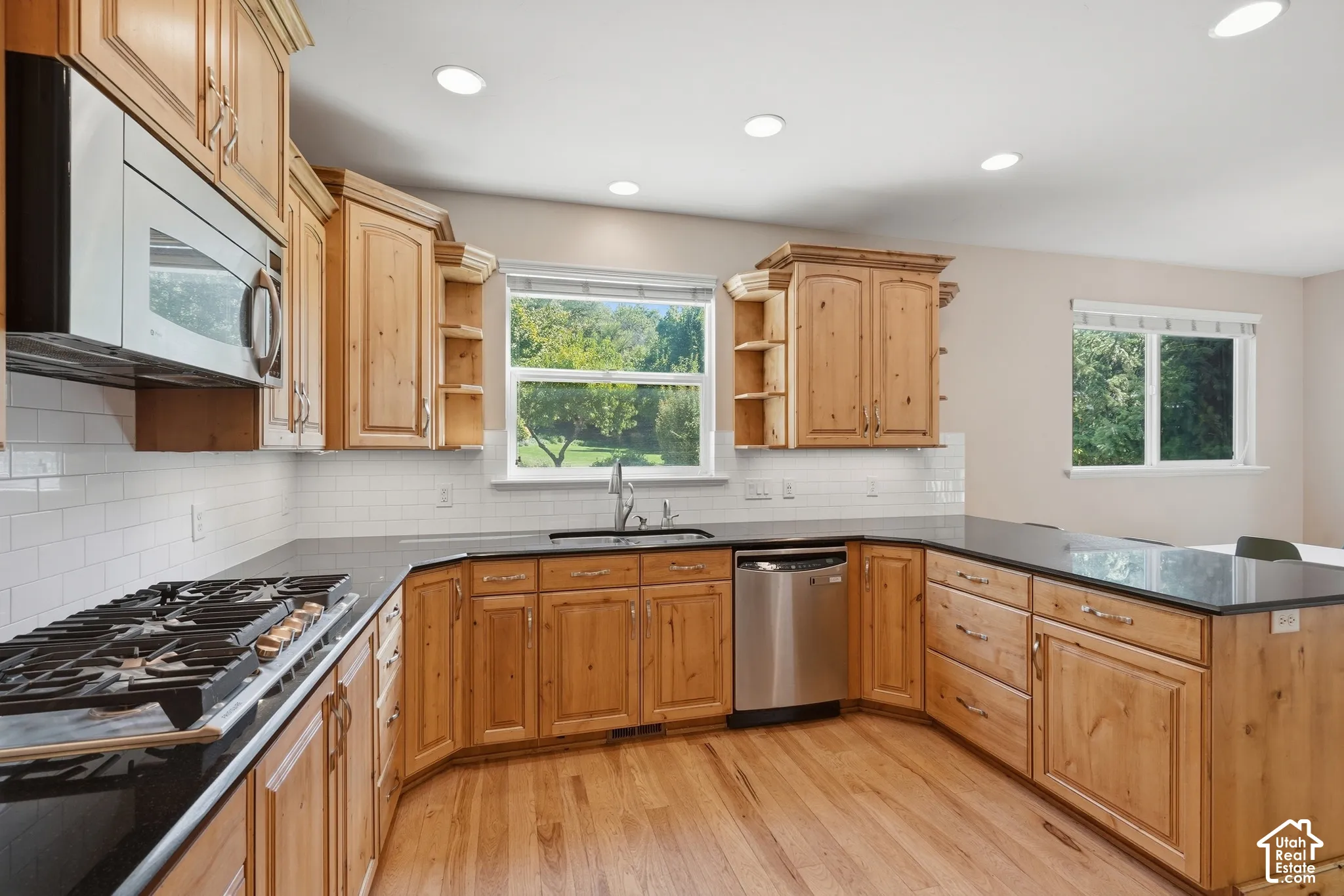 Spacious kitchen featuring wood-finish cabinetry, dark countertops, a stainless steel dishwasher, a built-in microwave, and recessed lighting
