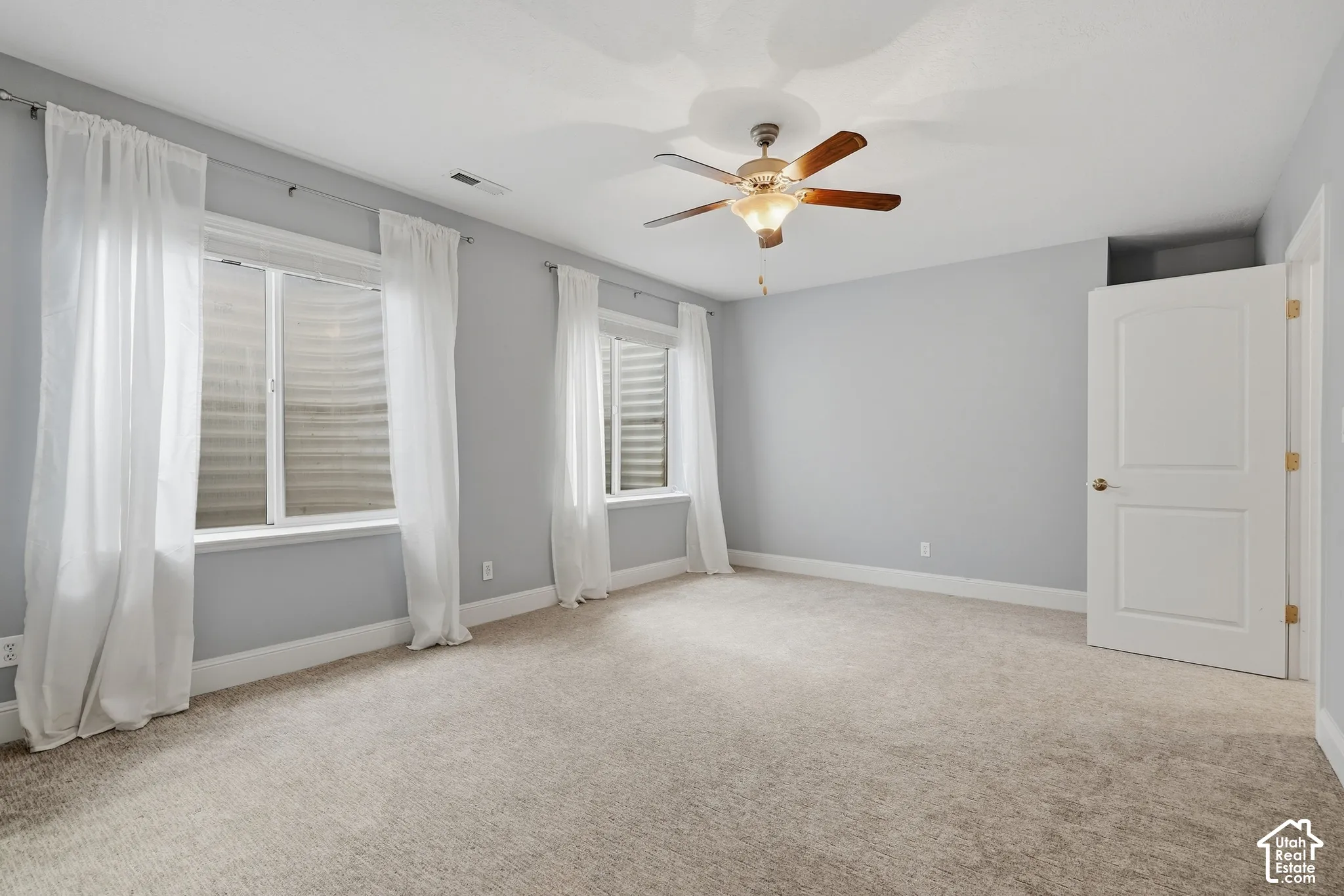 Neutral-toned carpeting, two windows, and a ceiling fan with integrated lighting