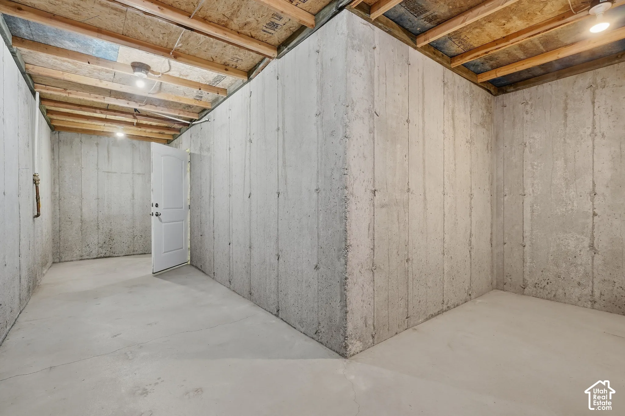 Unfinished basement with concrete slab flooring, exposed ceiling joists, and a white interior door