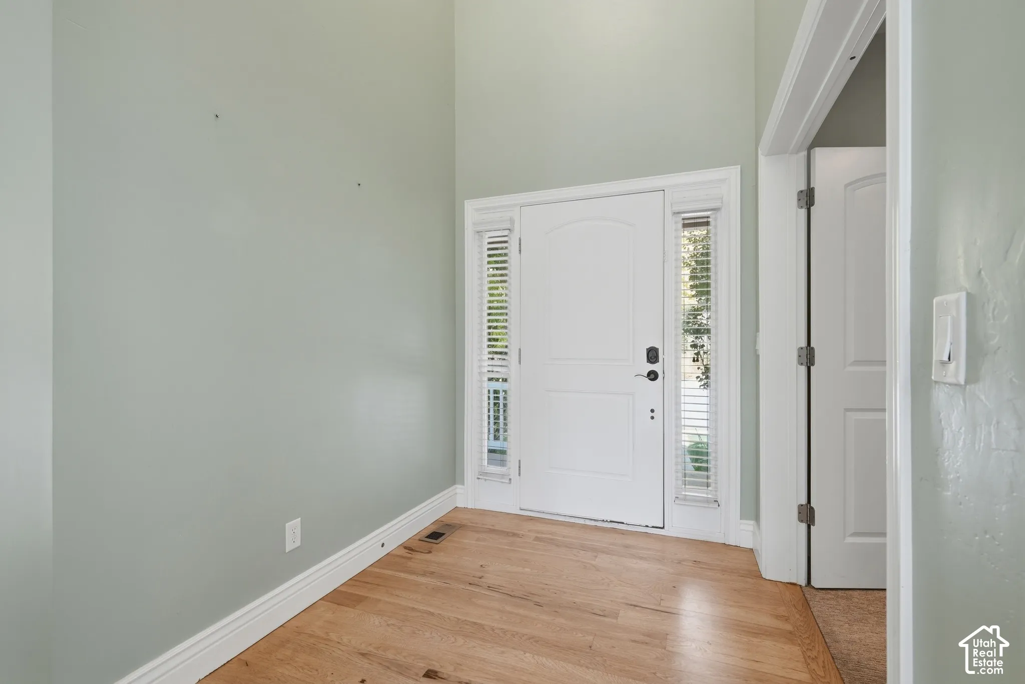 Arched entry door with sidelight windows, light wood-finish flooring, and a high ceiling