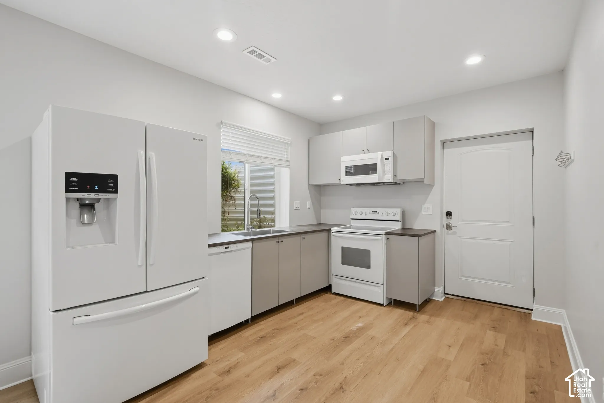 Contemporary kitchen featuring wood-finish flooring, recessed lighting, gray cabinetry, and white appliances