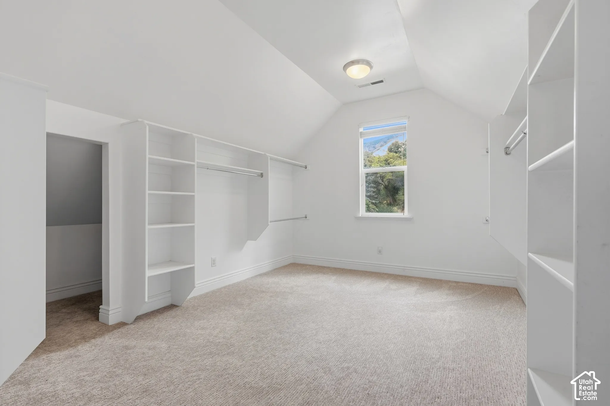 Sloped ceiling room featuring built-in shelving, hanging rods, an overhead light fixture, and a window