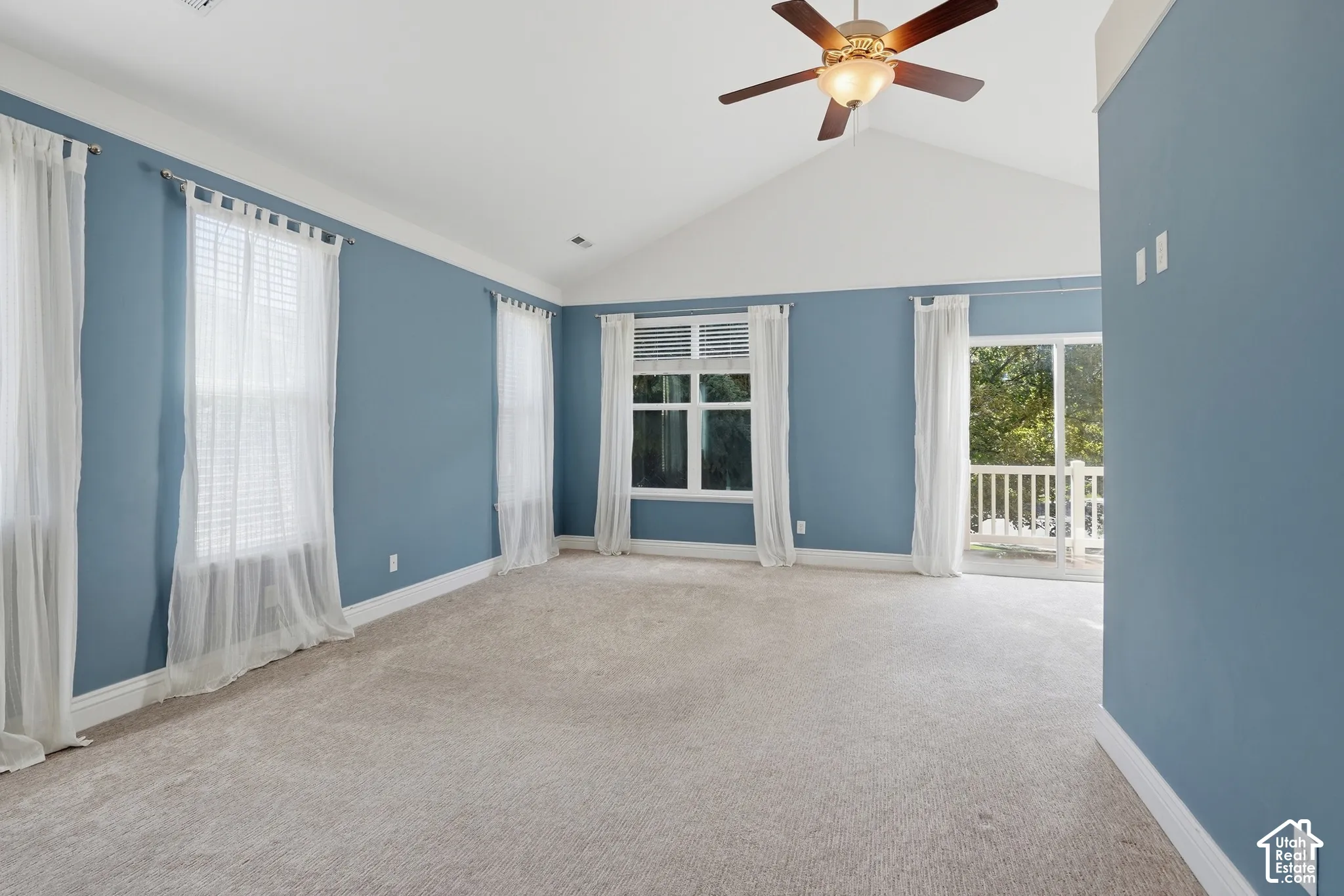 Vaulted ceiling, ceiling fan, carpeting, multiple windows, and a sliding glass door to a private balcony